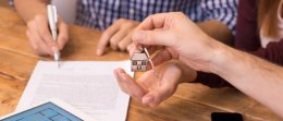 Happy young couple getting keys of their new house. Close up of female hand receiving keys from house broker. Closeup of the hand of a real estate agent who give the house keys to a woman while her boyfriend signing a contract.