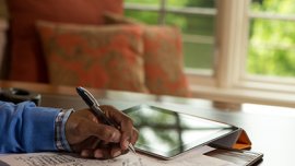 Man's writing on paper next to a tablet computer